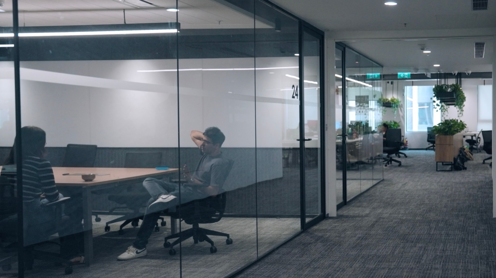 The glass meeting room from the corridor: glass on every side, reflecting the office
