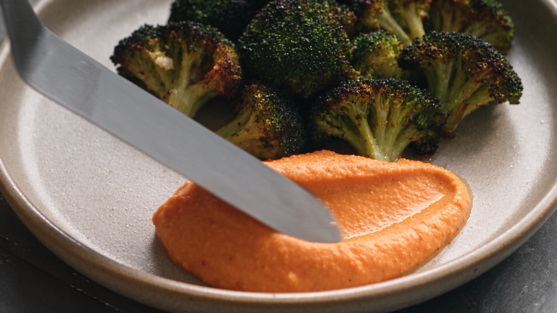 A knife spreads red pepper purée