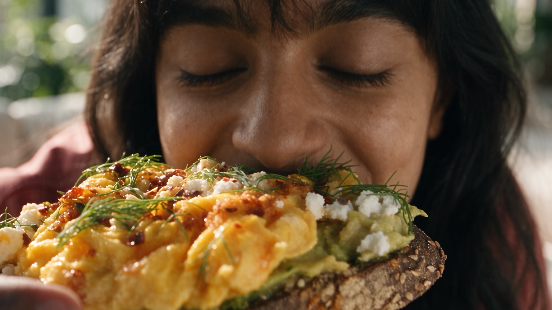 Eyes closed, she takes a bite of avocado and egg toast