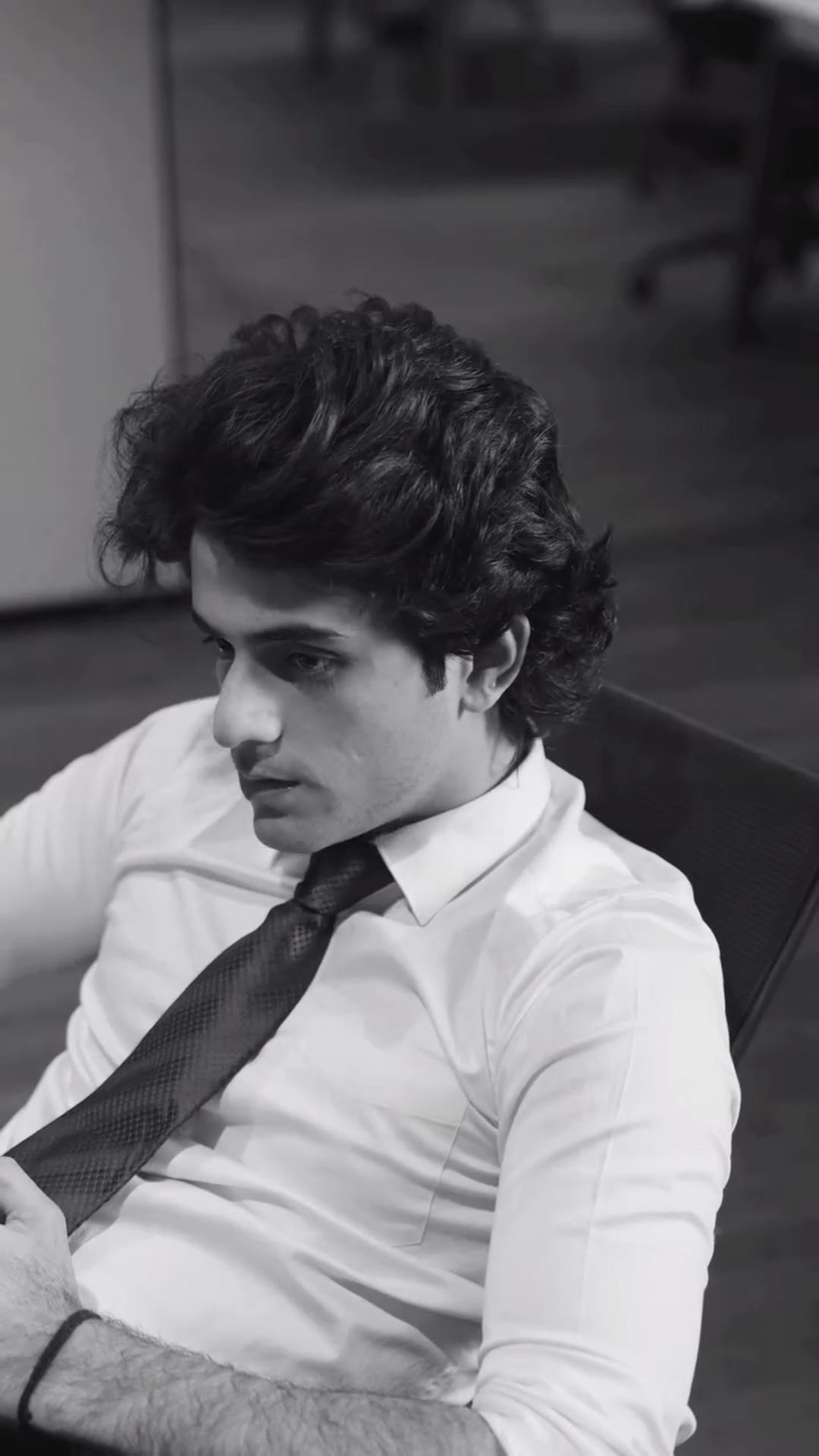 In a shirt and tie, leaning back at his desk